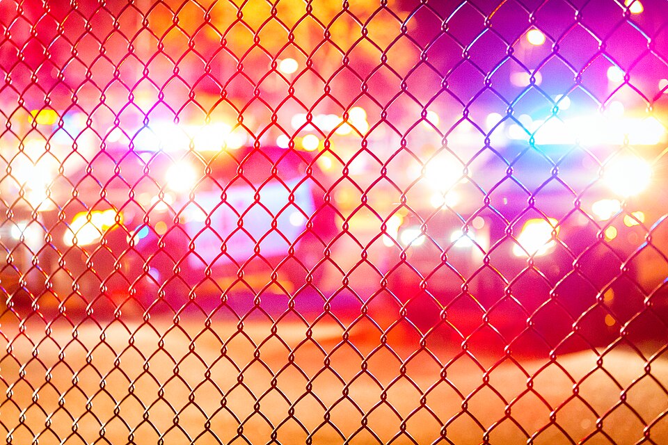 Police lights seen through a chain-link fence at night